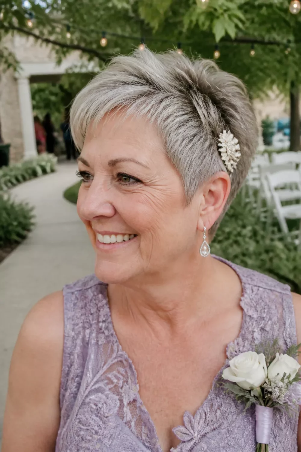 Short mother of the bride hairstyle: textured gray pixie with pearl floral pin at an outdoor wedding.