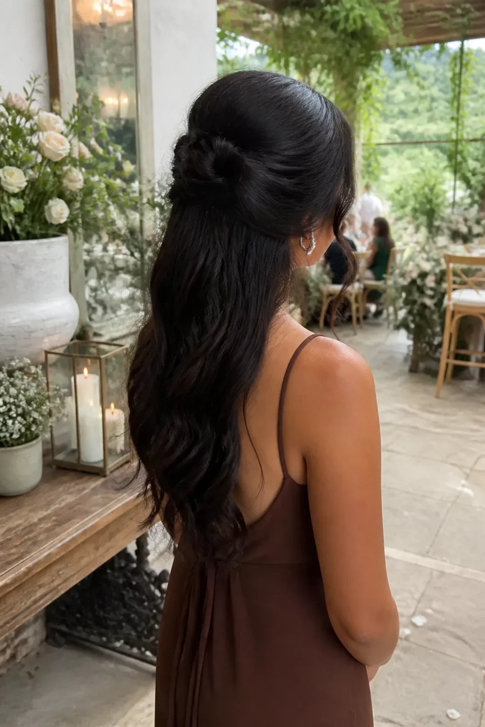 Wedding guest hairstyles for dark hair: half-up twisted knot with loose waves at an outdoor garden reception.