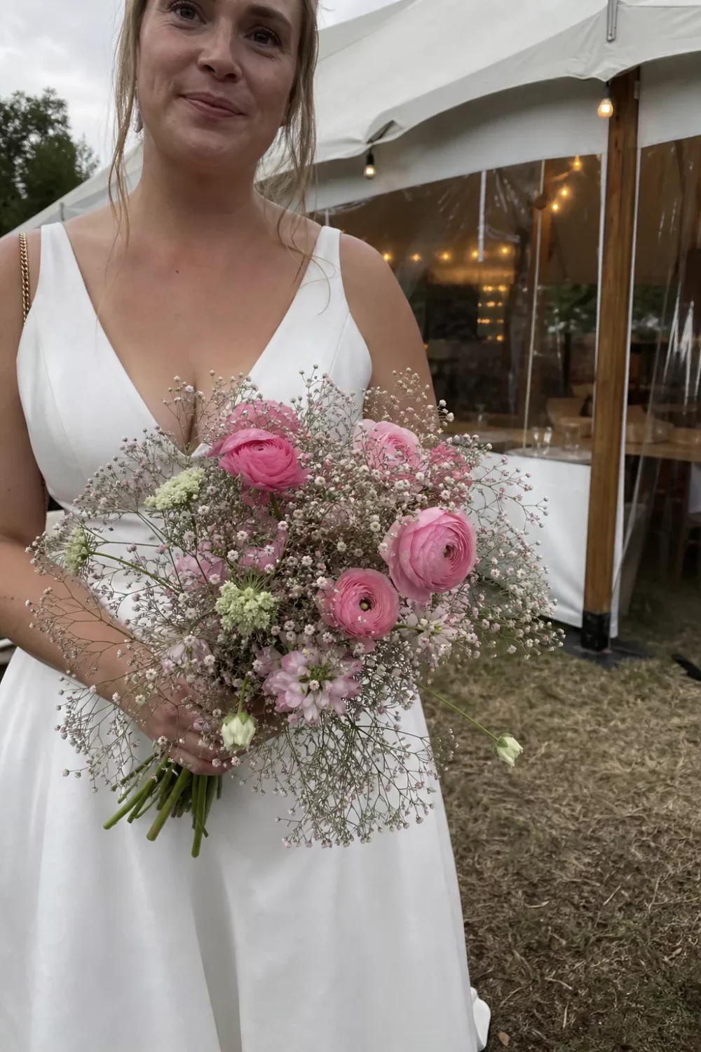 Bride holding pink wedding bouquet with ranunculus and baby's breath under a tent