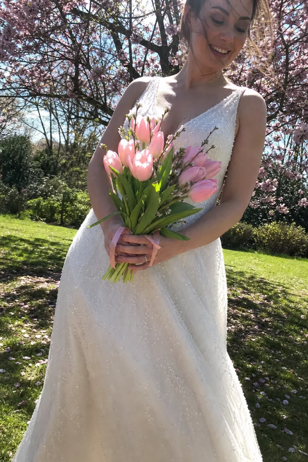 Bride holding a pastel pink tulip wedding bouquet among spring blossom trees
