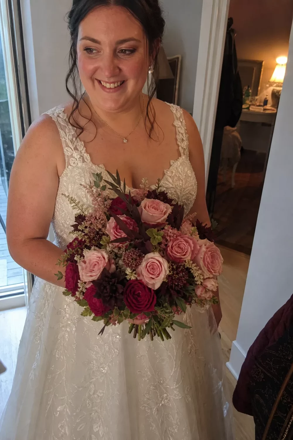 Bride holding a pink wedding bouquet with deep burgundy dahlia accents indoors