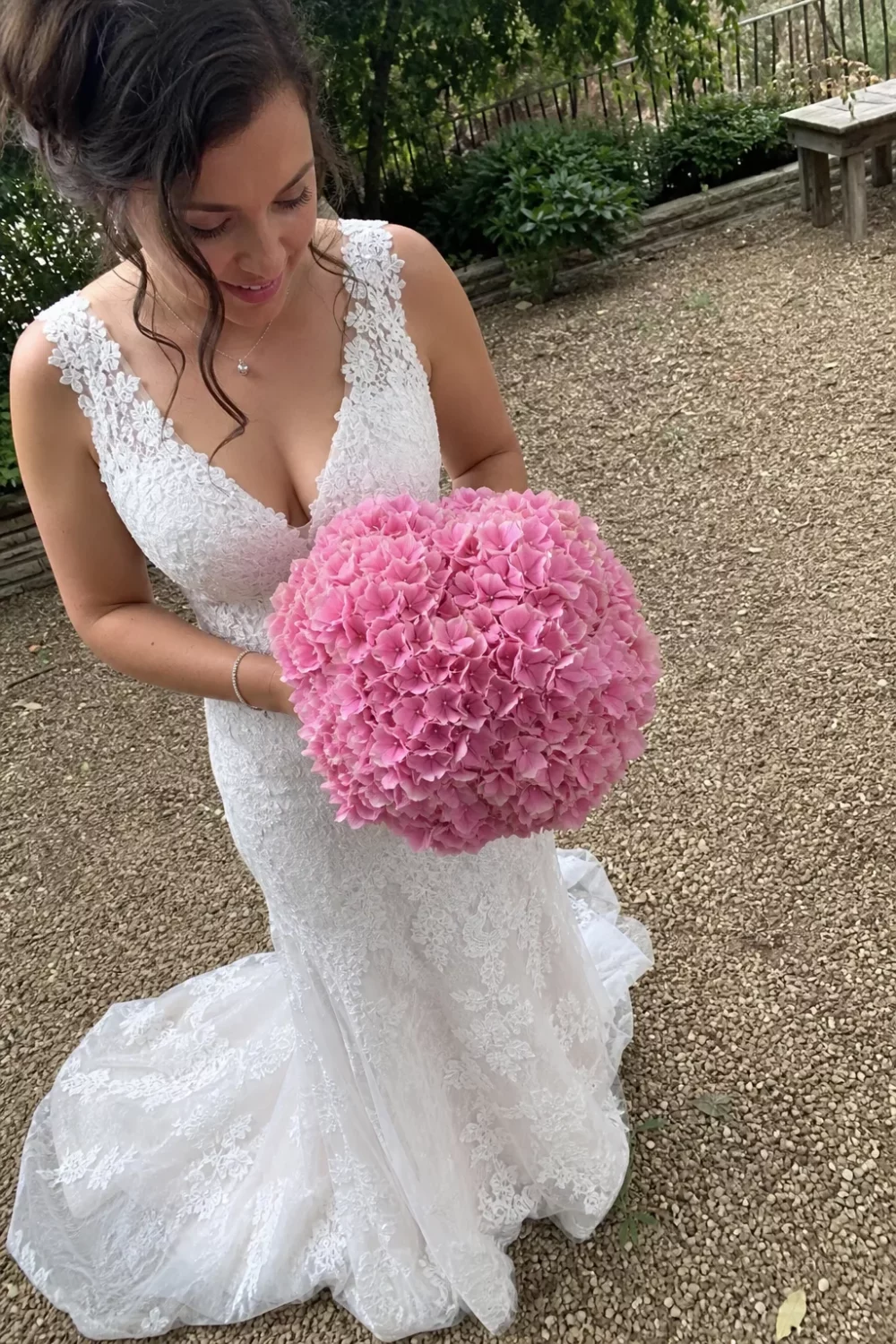 Bride holding a full pink hydrangea wedding bouquet on a garden gravel path