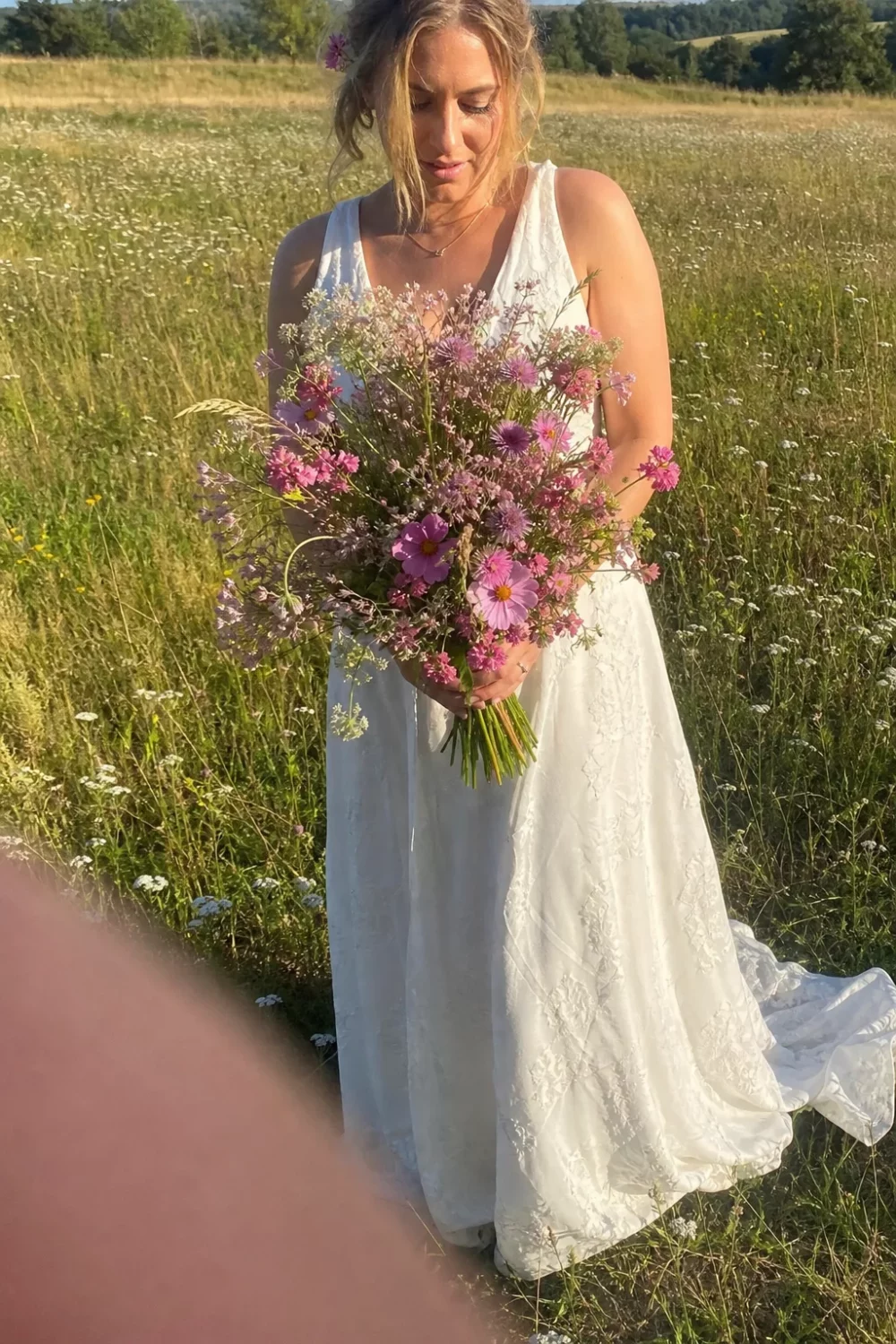 Bride holding a loose pink wildflower wedding bouquet in a meadow