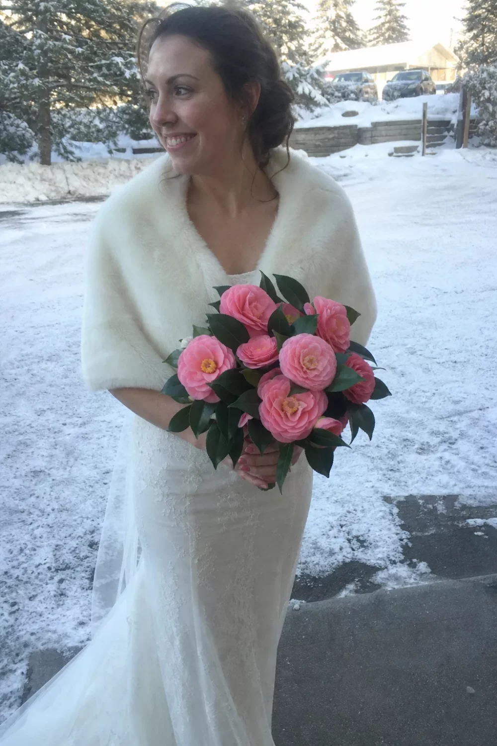 Bride holding pink camellia wedding bouquet in a snowy winter setting