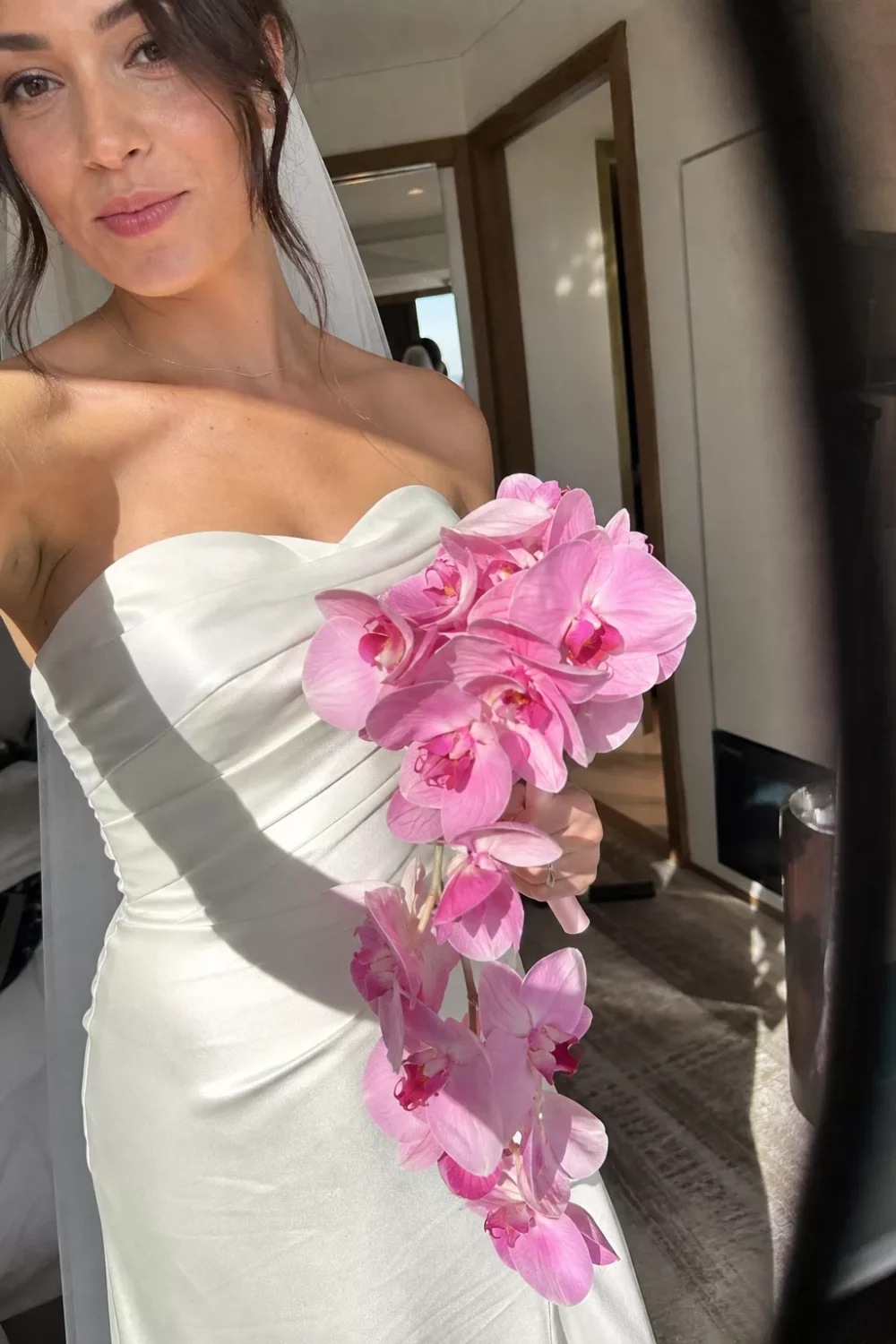 Bride holding a trailing pink orchid wedding bouquet in a hotel suite