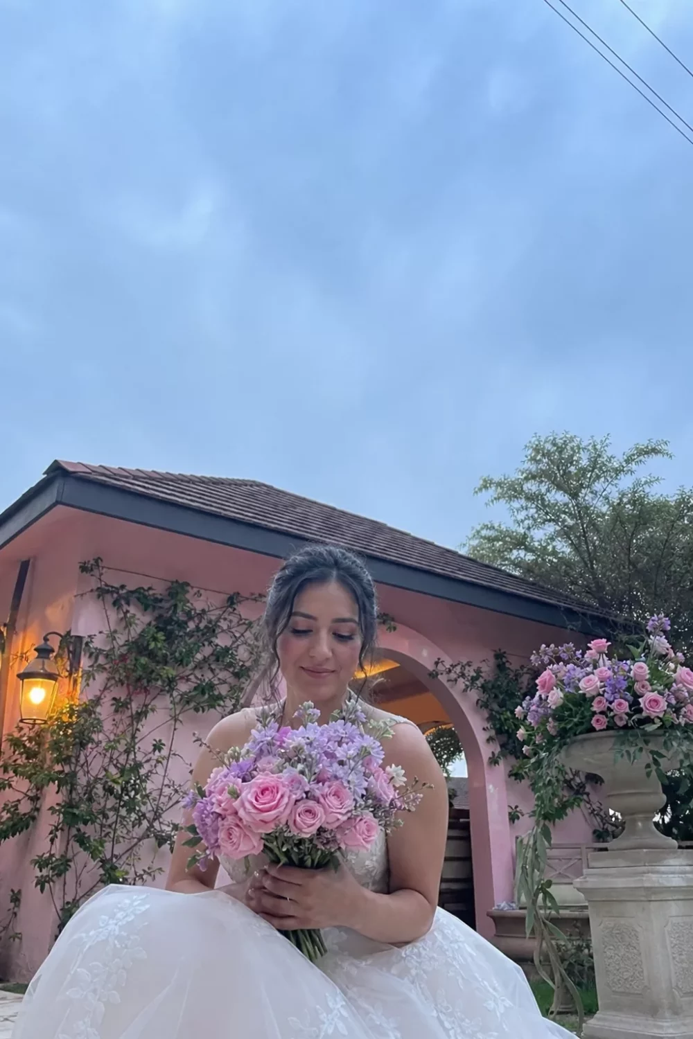 Bride holding a pink and lavender pastel wedding bouquet outdoors at dusk