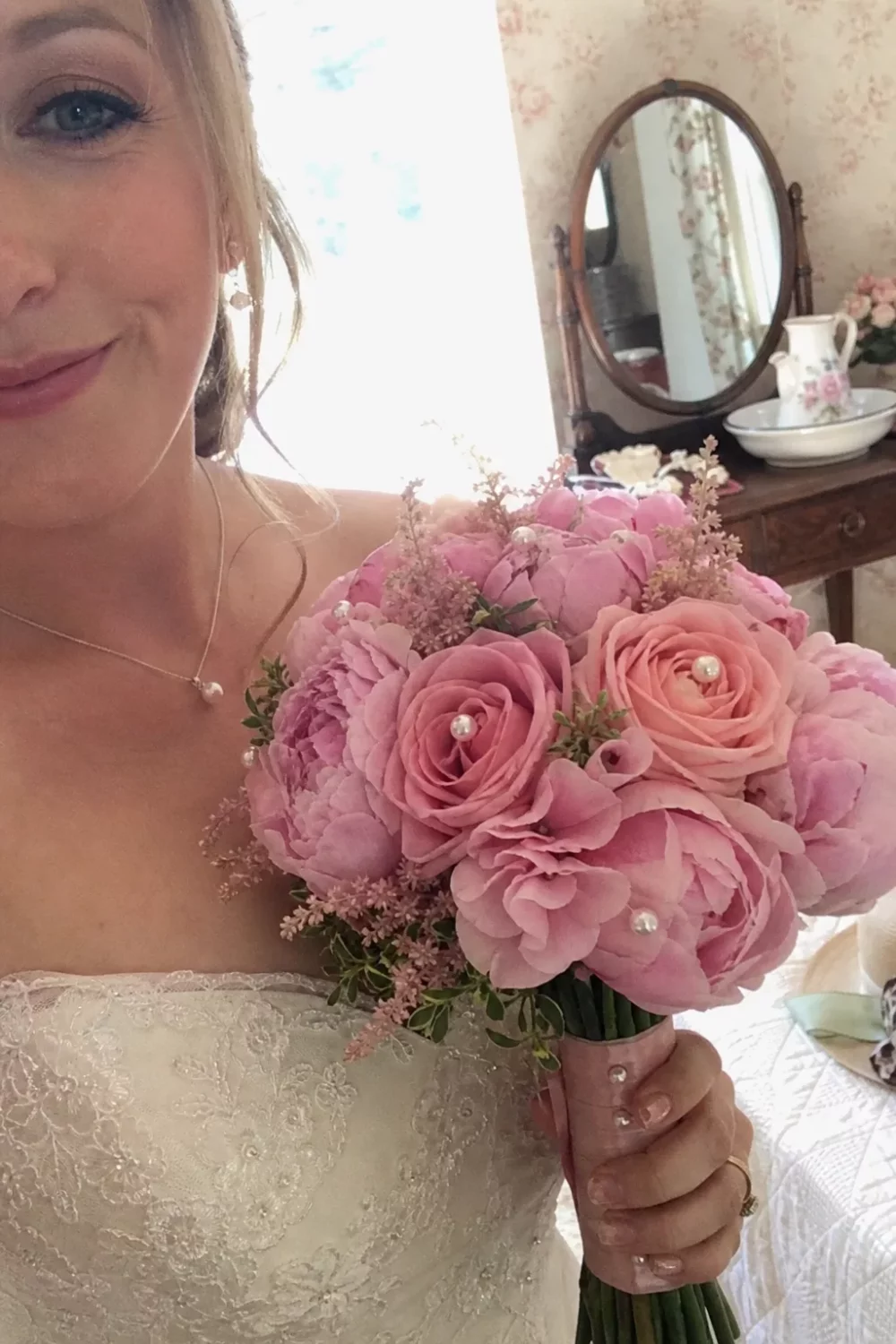 Bride holding a pink wedding bouquet with pearl pin details tucked among the roses