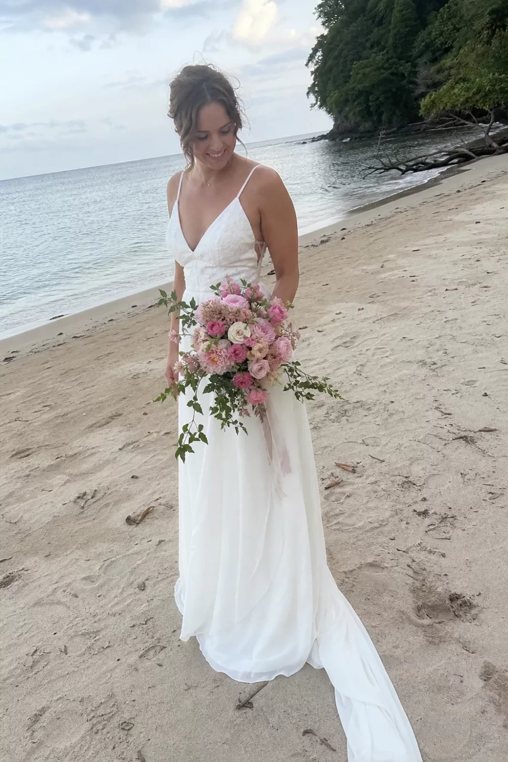 Bride holding a pink wedding bouquet with trailing ribbon on a beach shoreline