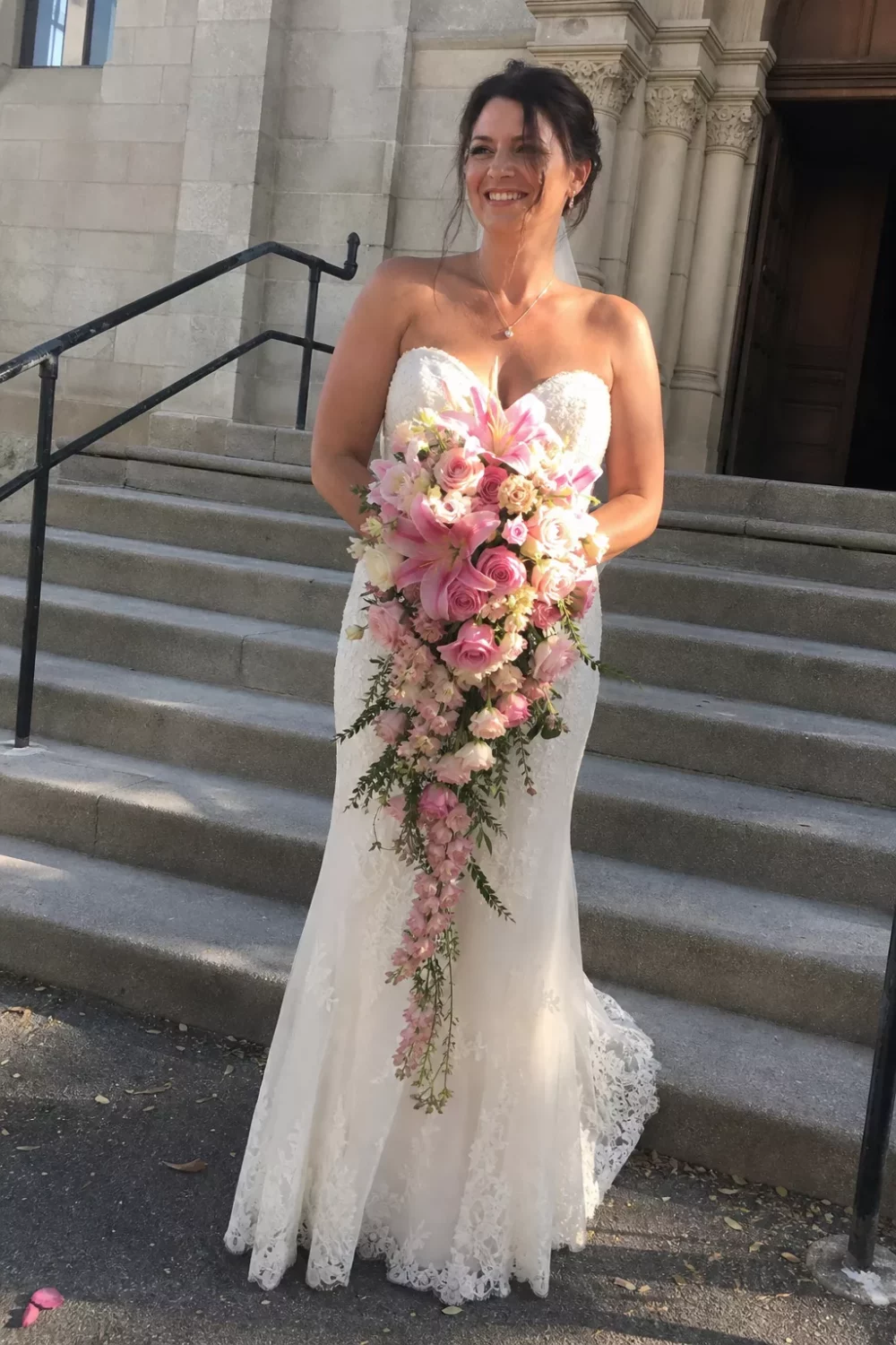 Bride on church steps holding a cascading pink wedding bouquet of roses and lilies