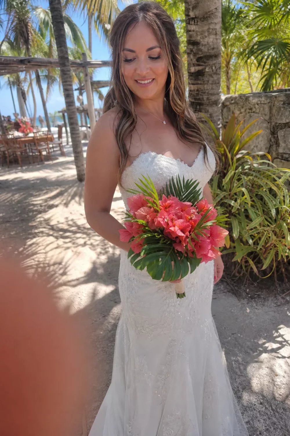Bride holding a coral pink wedding bouquet with tropical monstera leaf accents